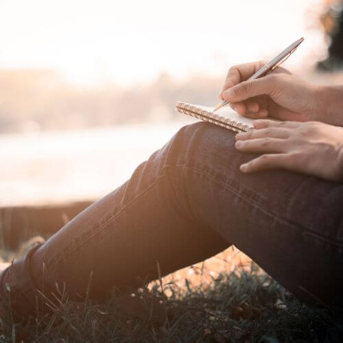 person writing on a notepad on her knees